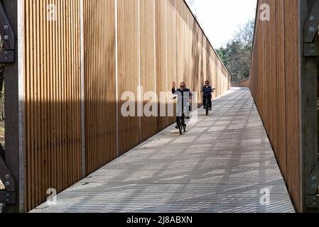 Maasmechelen, Limburg, Belgio - 04 12 2022 - Coppia matura che scende lungo un ponte di legno per i ciclisti Foto Stock