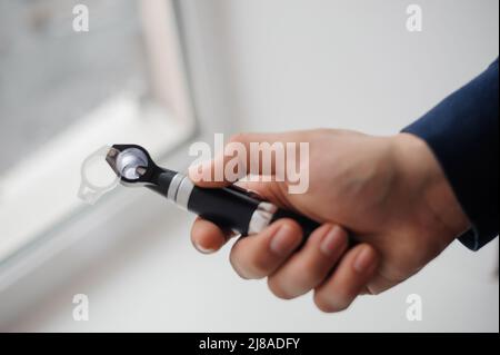 Otoscopio su sfondo nelle mani di un otolaringologo. Strumento per l'esame dell'orecchio e dell'orecchio medio Foto Stock
