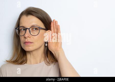 Una donna è dura nell'udito, tenendo la mano all'orecchio. Foto Stock