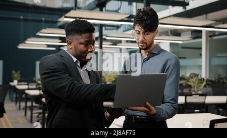 Due uomini business partner uomini uomo arabo in possesso di un laptop che mostra presentazione imprenditore africano guardando lo schermo computer colleghi di lavoro Foto Stock