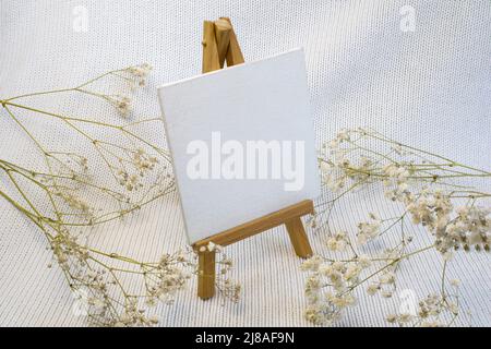 Cavalletto per artisti in miniatura su sfondo bianco lavorato a maglia. Art minimal concept close up Foto Stock