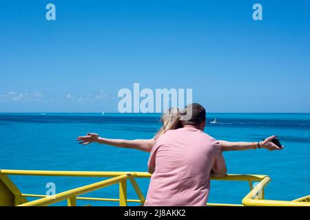 Vista posteriore di una coppia con le braccia distese in una nave contro il cielo blu, Isla Mujeres Messico Foto Stock