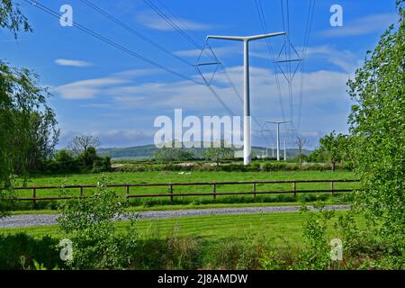 Bridgwater, Regno Unito. 13th maggio 2022. In un pomeriggio di sole ventoso e caldo, i primi piloni di energia elettrica New Shape T appena installati sono visti attraverso il paesaggio verde di Rooksbridge nel Somerset Nord, che viene messo a fornire energia dalla rete Nazionale. Picture Credit: Robert Timoney/Alamy Live News Foto Stock