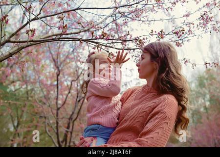 Madre e bambina, in piedi nel parco sotto un albero di fiori Foto Stock