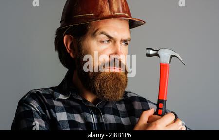 Costruttore in elmetto con martello. Ritratto di operaio barbuto in hardhat. Edificio. Riparazione. Foto Stock