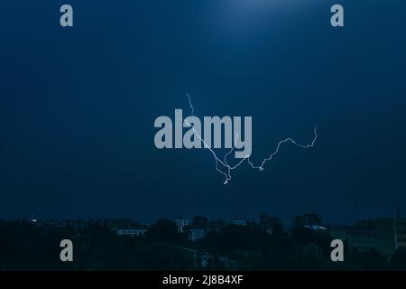 Fulmine nel cielo sopra la città. Luce lampeggiante nelle ore notturne scure. Thundernubi e scariche elettriche nell'atmosfera. Paesaggio urbano notturno. Foto Stock