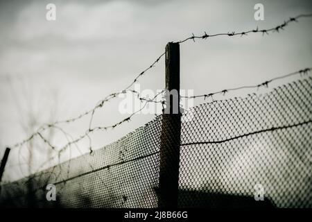 C'è una vecchia recinzione con un terribile filo spinato sullo sfondo di un cielo grigio triste coperto. Guerra e prigione. Foto Stock