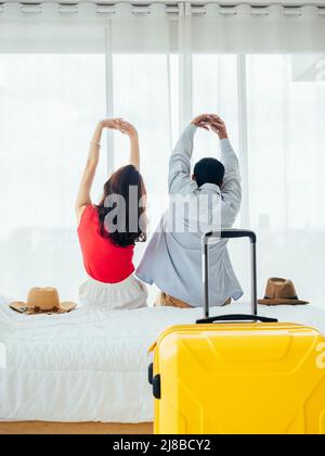 Coppia di turisti, felice vacanza. Vacanze estive. Vista posteriore del giovane uomo asiatico e donna che si allunga con relax sul letto con valigia vicino tenda Foto Stock
