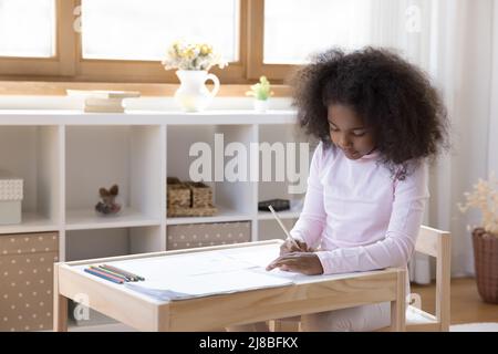 Carino preschool africano ragazza disegno seduto al tavolo in asilo nido Foto Stock