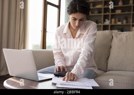 La donna calcola le spese sulla calcolatrice, paga le fatture usando il laptop Foto Stock