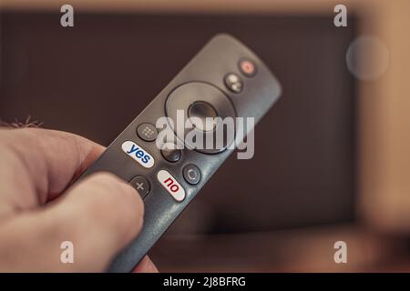 Telecomando TV a portata di mano con etichette sì e no. La scritta No in rosso e la scritta Sì in blu sui tasti del telecomando del televisore. Foto Stock