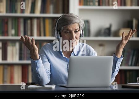 Insegnante senior impegnato in cuffie dando lezioni online Foto Stock