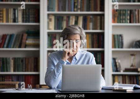 Una donna d'affari positiva e focalizzata con un computer portatile al tavolo Foto Stock