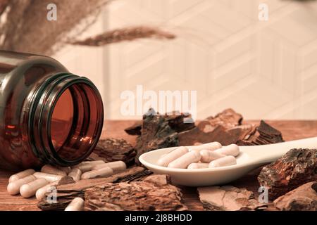 Cucchiaio con pillole dietetiche naturali sparse dalla bottiglia marrone. Tavolo di legno in cucina Foto Stock