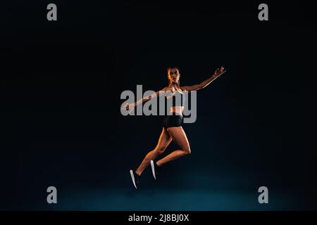 Donna sottile che lavora su sfondo nero. Atleta femminile che fa salti in studio. Foto Stock