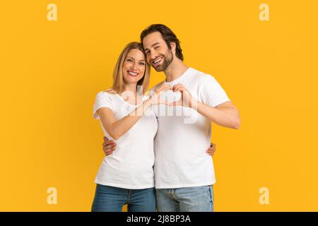 Felice attraente millennial europea moglie e marito con stubble in magliette bianche fare il cuore con le mani Foto Stock