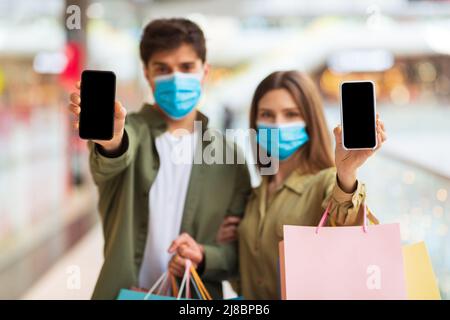 Maschere di coppia in faccia che mostrano gli schermi dei telefoni che Shopping in Hypermarket Foto Stock