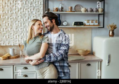 Soddisfatto giovane europeo maschio abbracciando sua moglie in cucina moderna interno. Amore, rapporto e romantico Foto Stock