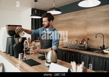 Il barista macina i chicchi di caffè prima di preparare il caffè Foto Stock