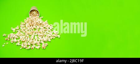 Il popcorn fuoriesce da una tazza di carta su uno sfondo verde in primo piano Foto Stock