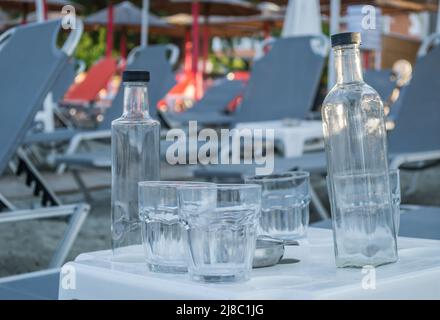 Un piccolo luogo turistico tranquillo Leptokarya in Grecia. Bottiglie d'acqua di vetro vuote, e bicchieri da bere lasciato su un tavolo in Grecia. Foto Stock