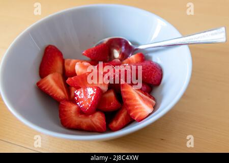 Molte fragole tagliate in ciotola sono pronte da mangiare con cucchiaio d'argento o come delizioso dito e snack sano con frutta rossa e vitamine su legno Foto Stock