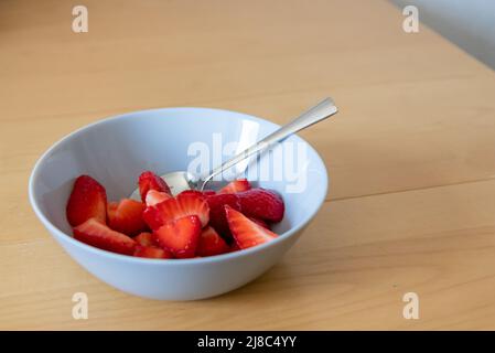 Molte fragole tagliate in ciotola sono pronte da mangiare con cucchiaio d'argento o come delizioso dito e snack sano con frutta rossa e vitamine su legno Foto Stock
