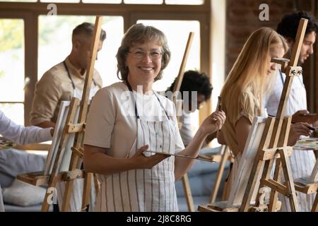 Donna matura in posa vicino al cavalletto con tavolozza e pennello Foto Stock