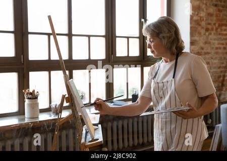 Pittura donna più anziana su cavalletto in officina Foto Stock