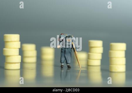 Fotografia di personaggi giocattolo in miniatura. Un vecchio uomo che cammina con bastone o crutch, nel mezzo di pillole di medicina. Concetto di accesso medico. Foto immagine Foto Stock