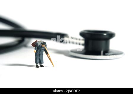 Fotografia di personaggi giocattolo in miniatura. Un vecchio uomo che cammina con bastone o crutch, di fronte allo stetoscopio. Concetto di controllo medico. Foto immagine Foto Stock