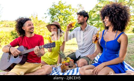 estate vacanze picnic all'aperto. multirazziale gruppo di amici mangiare e bere birre che posano su una coperta in un giardino parco. persone happy hour en Foto Stock