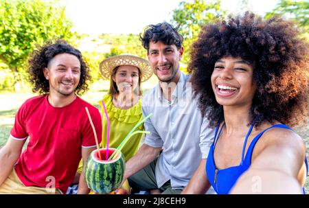 vacanze estive picnic all'aperto. multirazziale gruppo di amici che bevono di cocomero adagiato su una coperta in un giardino parco. persone happy hour en Foto Stock