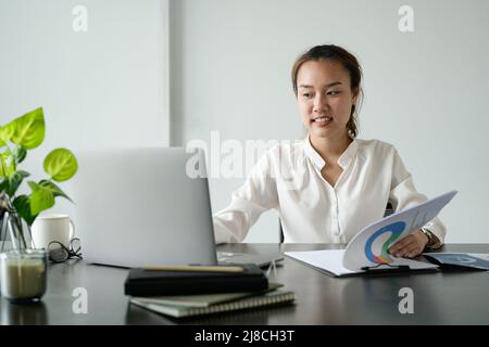 Giovane donna d'affari asiatica seduta sul suo posto di lavoro in ufficio. Giovane donna che lavora al notebook in ufficio Foto Stock