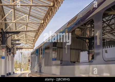 Treno in piedi presso una storica stazione ferroviaria piattaforma fiancheggiata da colonne. Un cielo limpido è sopra. Foto Stock