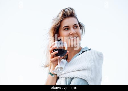 Ritratto di donna felice che tiene in mano bicchiere di vino e bere vino rosso su sfondo bianco primo piano, camminando lungo il terrapieno nella città resort a. Foto Stock