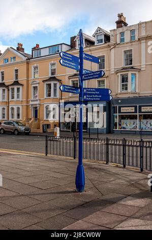 Un cartello bilingue con indicazioni stampate in lingua gallese e inglese si trova dietro le ringhiere metalliche all'angolo di una strada a Llandudno Foto Stock