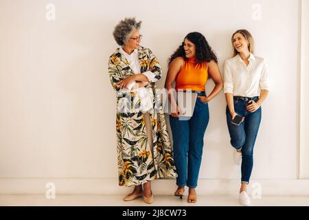 Gruppo di donne d'affari felici ridendo allegro mentre in piedi contro uno sfondo muro. Tre donne d'affari multiculturali che lavorano insieme in un al Foto Stock