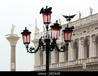 Vista romantica di un tipico lampione veneziano con colombe. Sullo sfondo, la Biblioteca Marciana e la colonna di San Teodoro avvolta nella nebbia Foto Stock