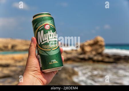 Ayia Napa, Cipro - 29 maggio 2021: La mano dell'uomo bianco tiene una lattina di birra Mythos Cypriot vicino con Ayia Napa spiaggia di resort estivo in background. Foto Stock