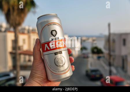 Ayia Napa, Cipro - 29 maggio 2021: La mano dell'uomo bianco tiene una lattina di birra di Leon primo piano, paesaggio urbano estivo resort sullo sfondo. La birra Leon è un prodotto Foto Stock