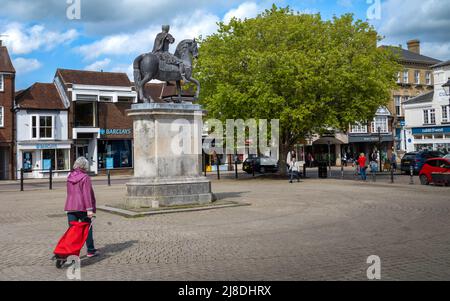 Una donna con un carrello per lo shopping cammina accanto alla statua di re Guglielmo III su un cavallo nella piazza della città di Petersfield in Hampshire, Inghilterra Foto Stock