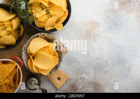 Spuntini. Cibo malsano. Tutti i classici spuntini di patate con arachidi, anelli di popcorn e cipolle e pretzel salati in ciotole su fondo grigio di cemento Foto Stock