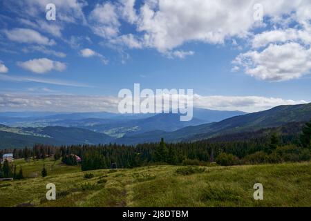 Piccolo villaggio di montagna, con pochi cottage in fitta foresta di conifere in autunno. Vista panoramica del villaggio remoto in montagna, con magnifico paesaggio sullo sfondo. Concetto di altopiano. Foto Stock