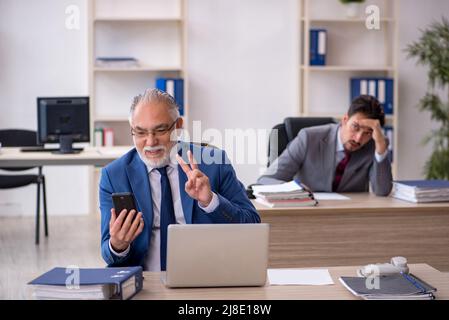 Due colleghi maschi seduti sul posto di lavoro Foto Stock