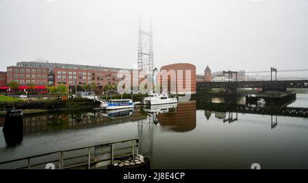 NORWALK, CT, USA - 15 MAGGIO 2022: Bella nebbia mattutina vicino al centro con acquario marittimo, barche e bricge railrod Foto Stock