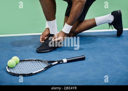 Primo piano di scarpe sportive nere irriconoscibili che legano le scarpe al campo da tennis, spazio copia Foto Stock