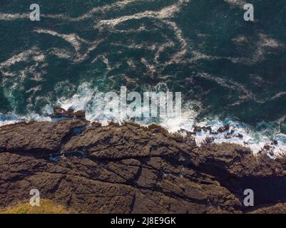 Riprese da un drone. Riva rocciosa dell'oceano e acqua turchese con onde bianche schiumose che battono contro la riva. Bella stagcape. Minimalismo. Abstrac Foto Stock