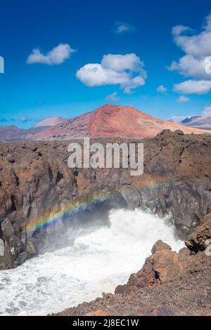 Bellissimo arcobaleno causato dallo schiantamento delle onde dell'Oceano contro le scogliere vulcaniche di Los Hervideros, Lanzarote, Isole Canarie, Spagna Foto Stock