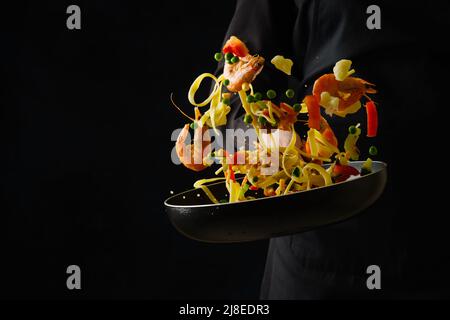 Un luminoso piatto festivo - un mix di frutti di mare, pasta italiana e verdure in una padella. Esplosione di colori e colori. Il processo di cottura dei frutti di mare Foto Stock